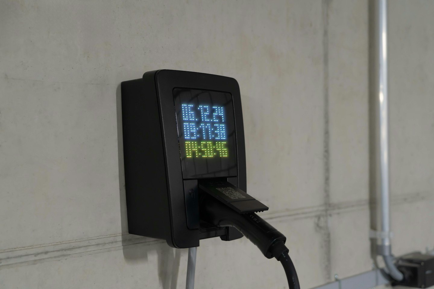 Black electric vehicle charging station mounted on a concrete wall.